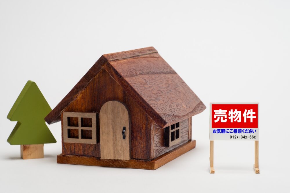 一戸建ての模型に売り物件の札が立っているイメージ